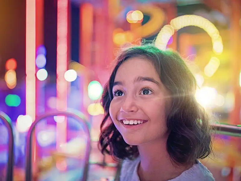 Une jeune fille sourit sur la grande roue d'un parc d'attractions.