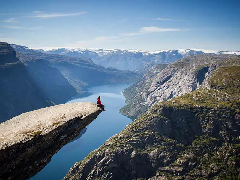 homme assis sur le rocher trolltunga au-dessus d'un fjord norvégien.