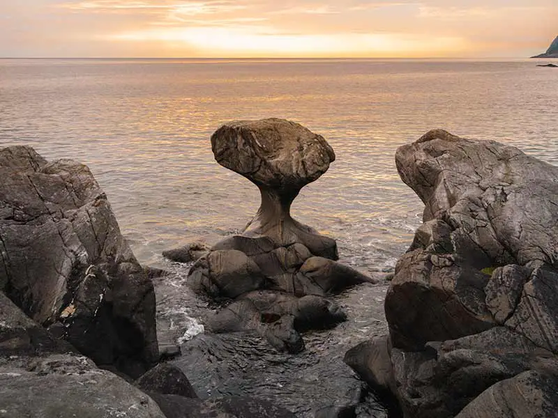 Pierre à la forme inhabituelle sur le rivage en Norvège avec le coucher du soleil en arrière-plan.