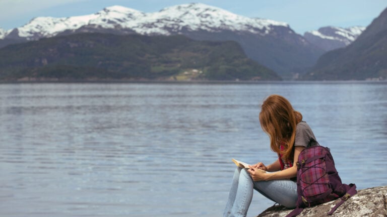 Fille lisant un livre scandinave au bord d'un fjord.