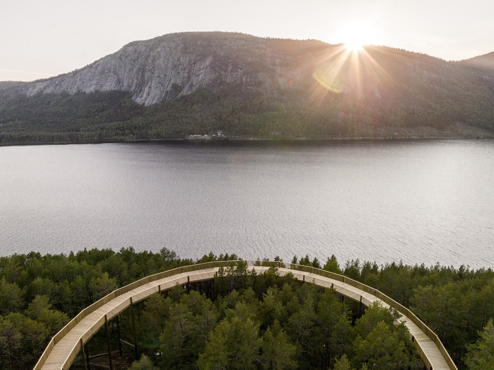 Une passerelle accessible dans les arbres à travers le parc Hamaren en Norvège 20 Photo aérienne d'une promenade sinueuse en pin au milieu d'une forêt près d'un lac et d'une colline escarpée.