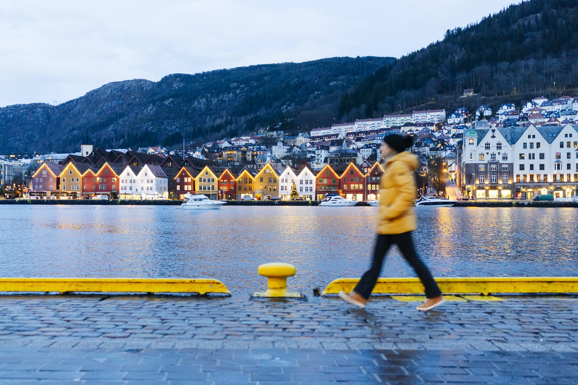 9 choses à savoir avant de visiter la Norvège 9 Une femme portant un chapeau et un manteau d'hiver marche le long d'un front de mer bordé de bâtiments colorés.