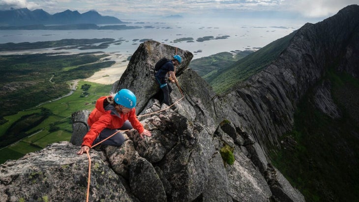 Voici les meilleures cabanes côtières de Norvège 20 Deux alpinistes franchissent le précipice de la traversée de Nordskot, avec une vue imprenable sur la mer grise et la vallée verdoyante en contrebas.