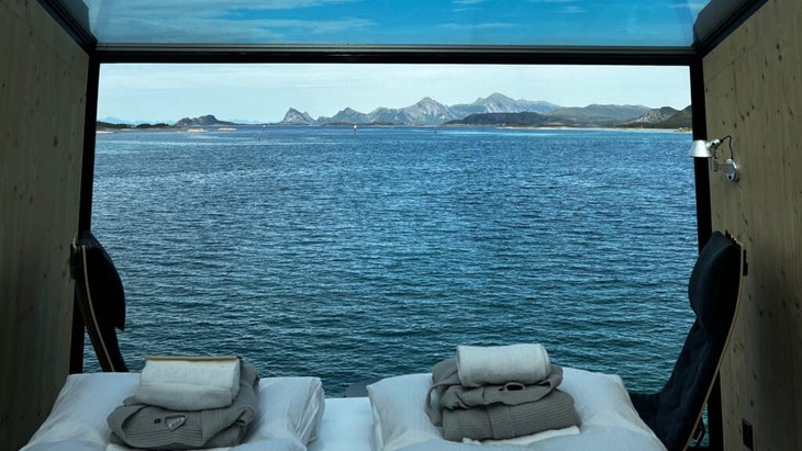 Voici les meilleures cabanes côtières de Norvège 21 L'intérieur du deuxième étage des nouvelles tours, avec un lit pour deux personnes, deux chaises noires et un plafond en verre. La vue donne sur la mer et les montagnes lointaines.