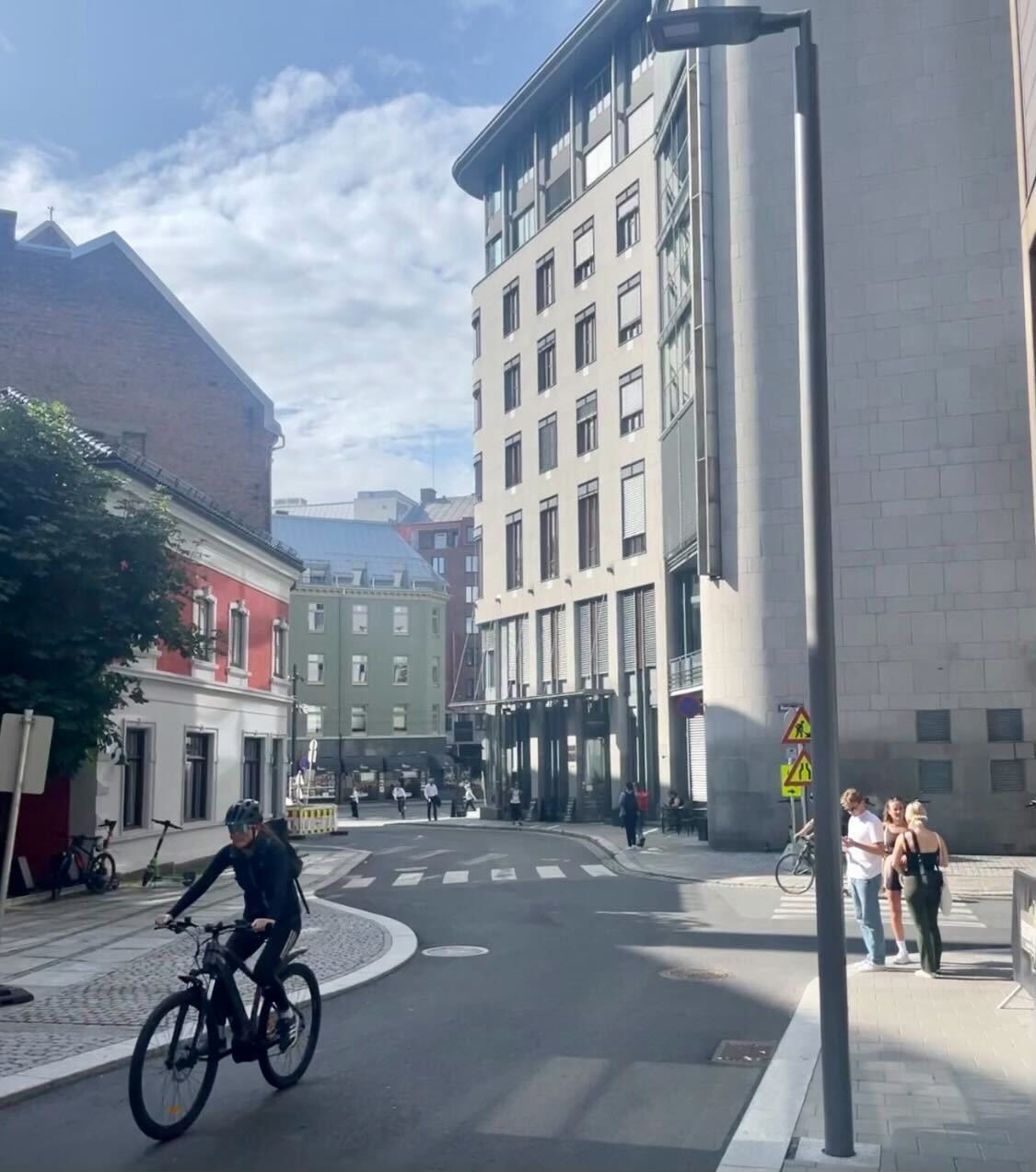 Pourquoi la Norvège repense-t-elle sa dépendance à l'égard des voitures électriques ? 14 Une rue étroite et sinueuse dans une zone urbaine avec des piétons et un cycliste visibles, mais pas de voitures.