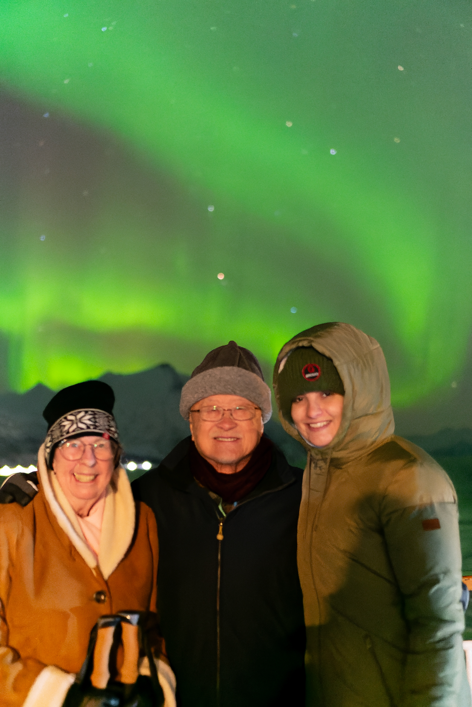Trois personnes souriant avec une aurore boréale dans le ciel derrière elles.