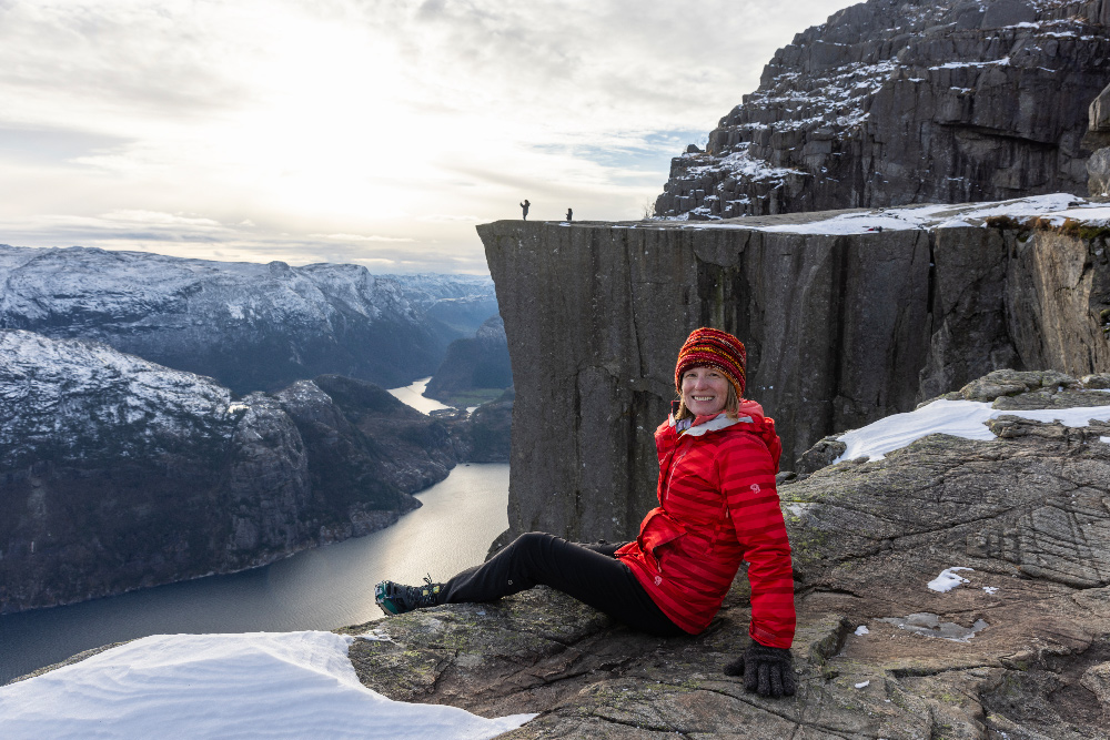 La Norvège en hiver : conseils d’experts pour des vacances magiques 17 Brook posant devant Pulpit Rock au-dessus du Lysefjord avec des montagnes voyantes en arrière-plan.