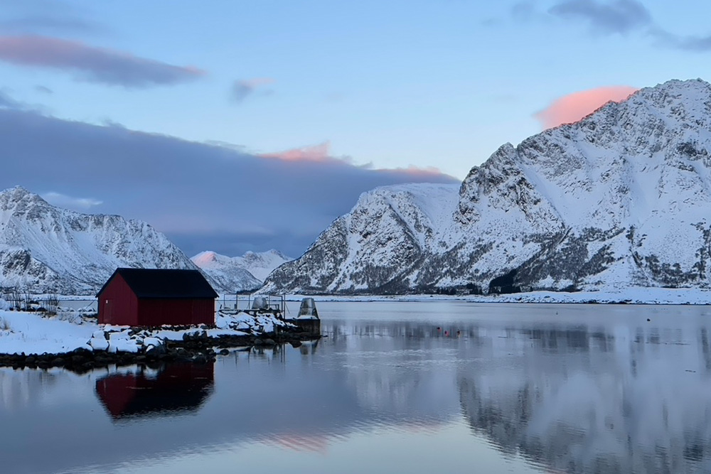 La Norvège en hiver : conseils d’experts pour des vacances magiques 20 Un paysage des îles Lofoten avec des montagnes enneigées, la mer de Norvège et une maison rorbu.