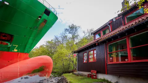 NTB/Jan Langhaugvia via Reuters La proue d'un porte-conteneurs vert et rouge à côté d'une petite cabine en bois