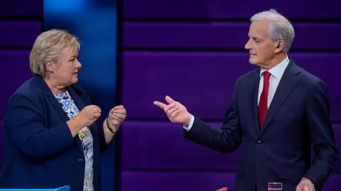 STIAN LYSBERG SOLUM/NTB/AFP Erna Solberg (à gauche), veste et robe bleu foncé, cheveux blonds, tient ses mains en avant tandis que son opposant porte une cravate rouge et une veste foncée à droite.