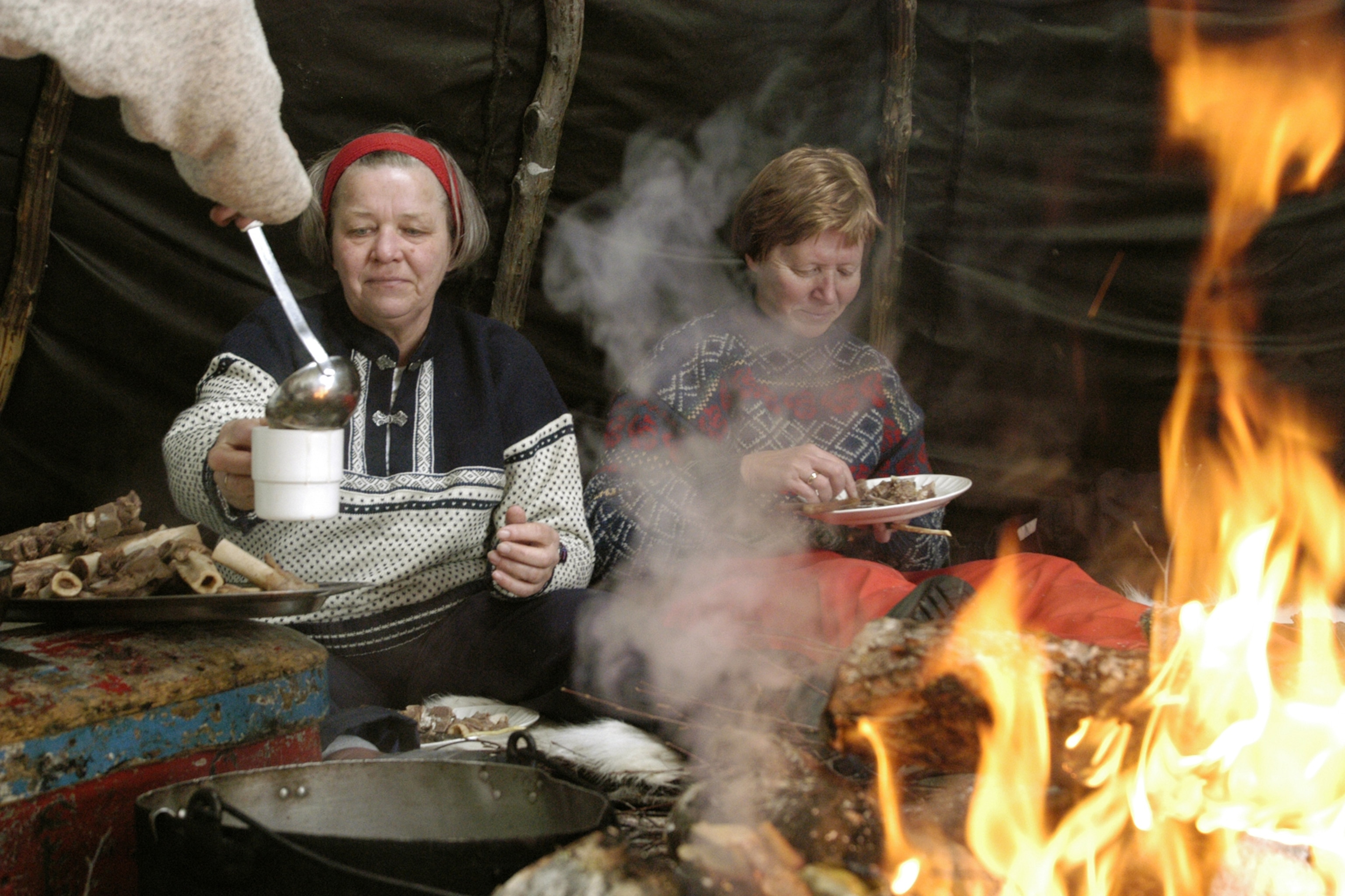 L'hiver dans le nord de la Norvège est l'aventure ultime - voici pourquoi 11 Deux femmes se font servir de la nourriture devant un feu de bois dans une tente du nord de la Norvège.
