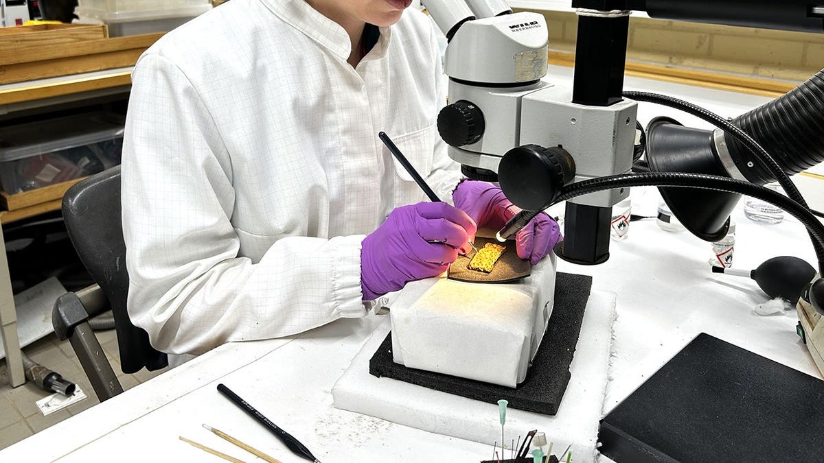 Un randonneur norvégien découvre une gaine d'épée en or vieille de 1 500 ans sous un arbre tombé 13 Une femme dans un laboratoire en train d'analyser un artefact en or